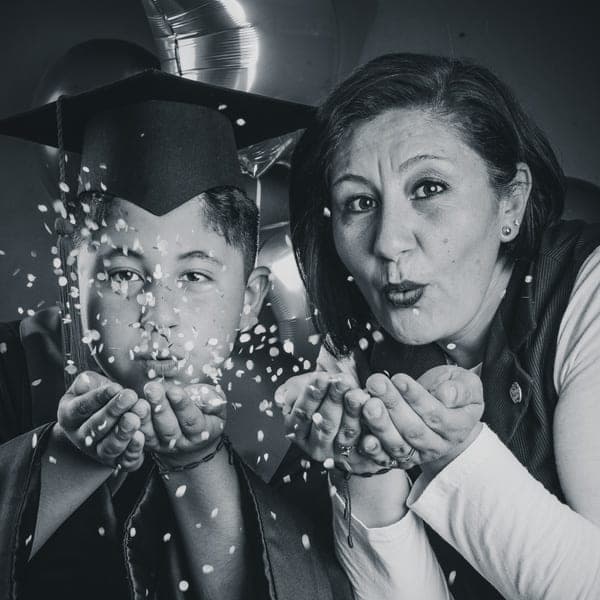 Un graduado y su mamá soplando confeti hacia la cámara el día de la graduación